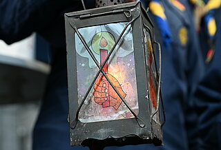 Lampe aus Metall, deren Scheiben mit einer Hand die eine Kerze hält bemalt sind.