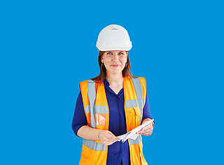 Frau mit Bauhelm und oranger Warnweste vor blaumen Hintergrund