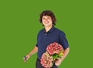 Mann steht mit Hortensien in der Hand vor grünem Hintergrund