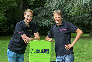 Zwei Männer, die sich auf einen grünen Würfel mit Schriftzug Ausbildung lehnen