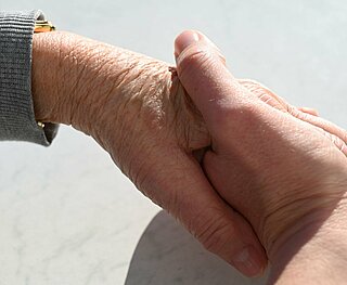 Eine Hand eines jungen Menschen hält die Hand einer älteren Person.