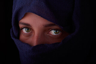 Frau mit Kopftuch und Schleier vor Gesicht, nur Augenpartie ist zu sehen. 