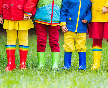 Kinder mit bunten Regensachen auf einer grünen Wiese