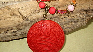 Das Bild zeigt eine rote Halskette mit Perlen und Anhänger.