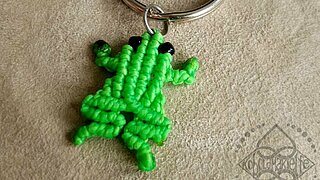Das Bild zeigt einen Schlüsselanhänger aus Makramee mit grünem Frosch.
